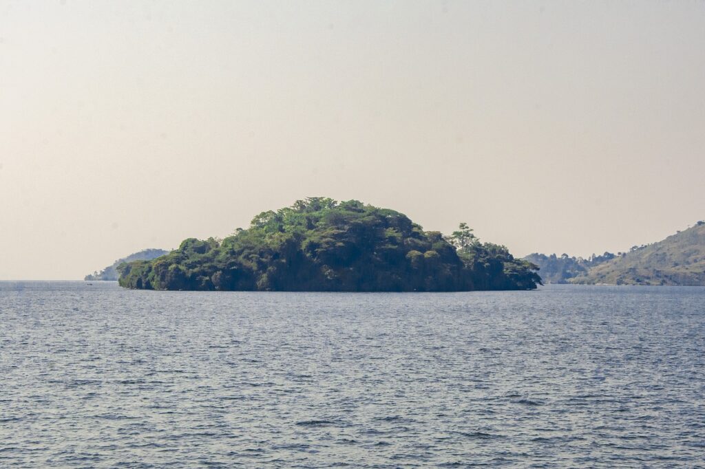 An island covered in lush greenery sits in the middle of a serene lake with mountainous terrain in the background.