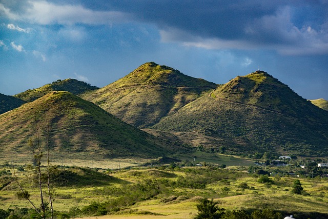 A scenic view of green hills with patches of sunlight casting shadows on their slopes.